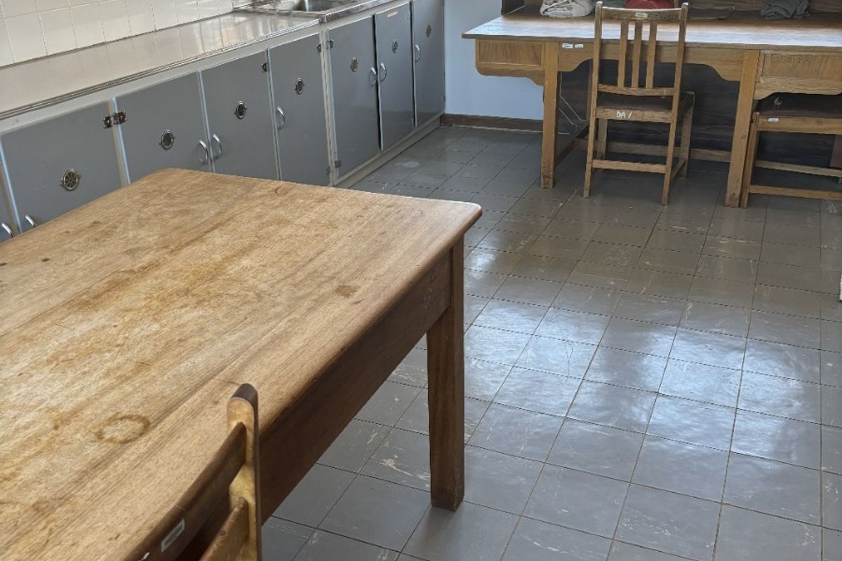 A functional commercial kitchen space featuring built-in cabinetry, a stainless steel sink, tiled backsplash, and durable tiled flooring with security bars on the windows.