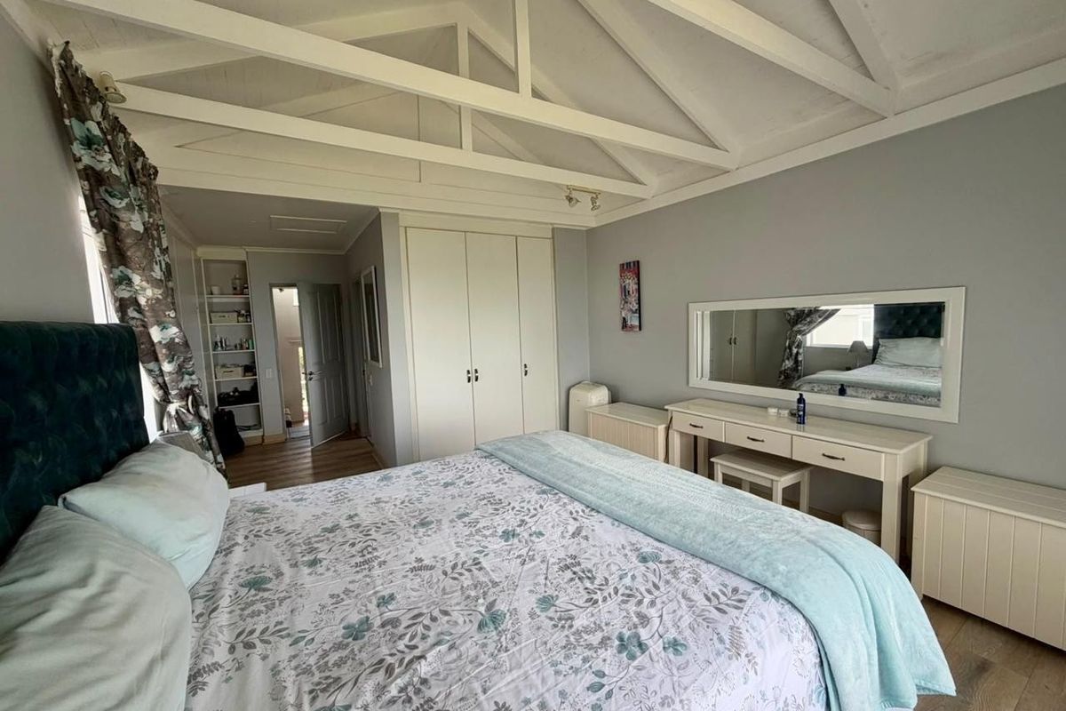 Spacious bedroom featuring a vaulted ceiling with exposed rafters, built-in cupboards, and durable laminate flooring, offering a bright and airy atmosphere.