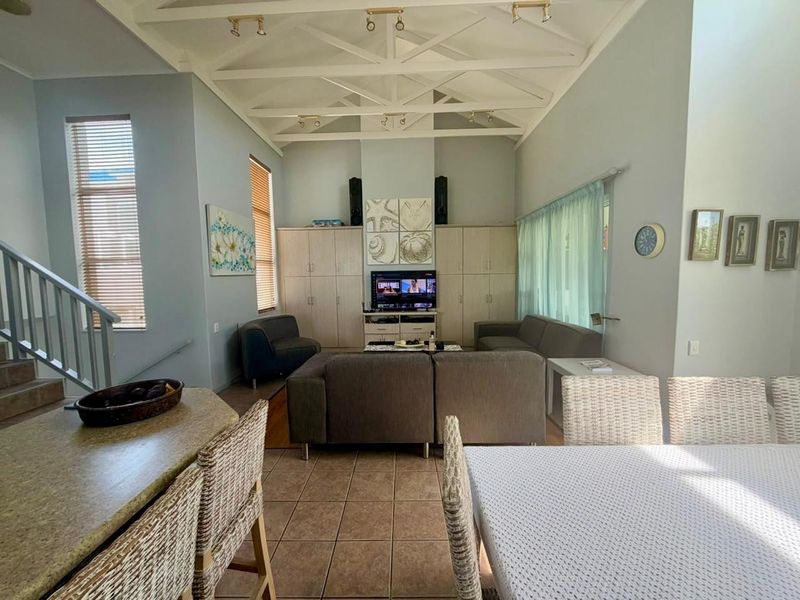 Spacious open-plan living area featuring a high vaulted ceiling with exposed trusses, built-in storage cabinetry, and tiled flooring throughout.