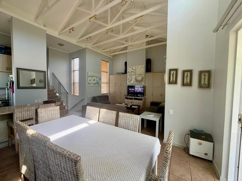 Spacious open-plan living and dining area featuring high vaulted ceilings with exposed trusses, built-in cabinetry, and tiled flooring.