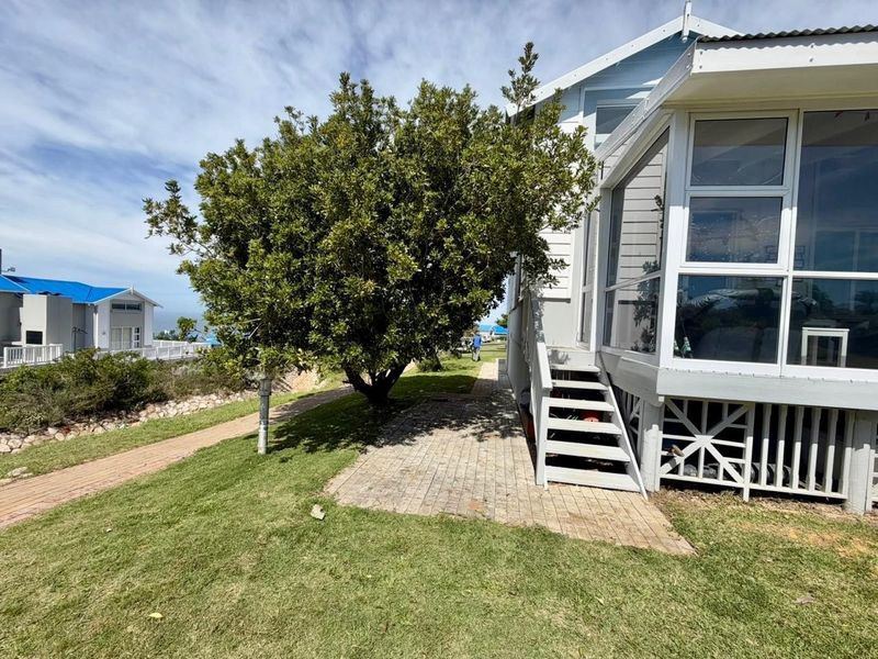 Rear exterior view of the property featuring a raised enclosed sunroom, timber staircase, and paved garden path set within a landscaped yard.