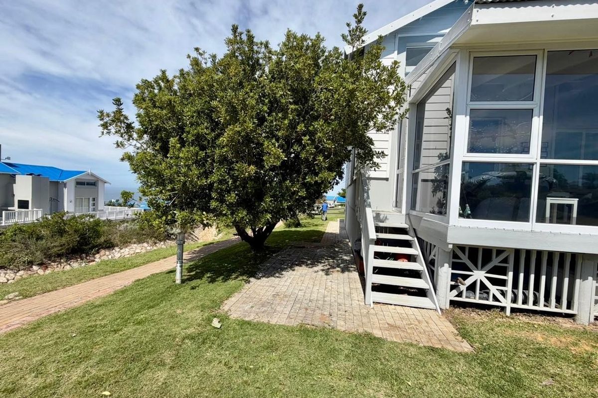 Rear exterior view of the property featuring a raised enclosed sunroom, timber staircase, and paved garden path set within a landscaped yard.
