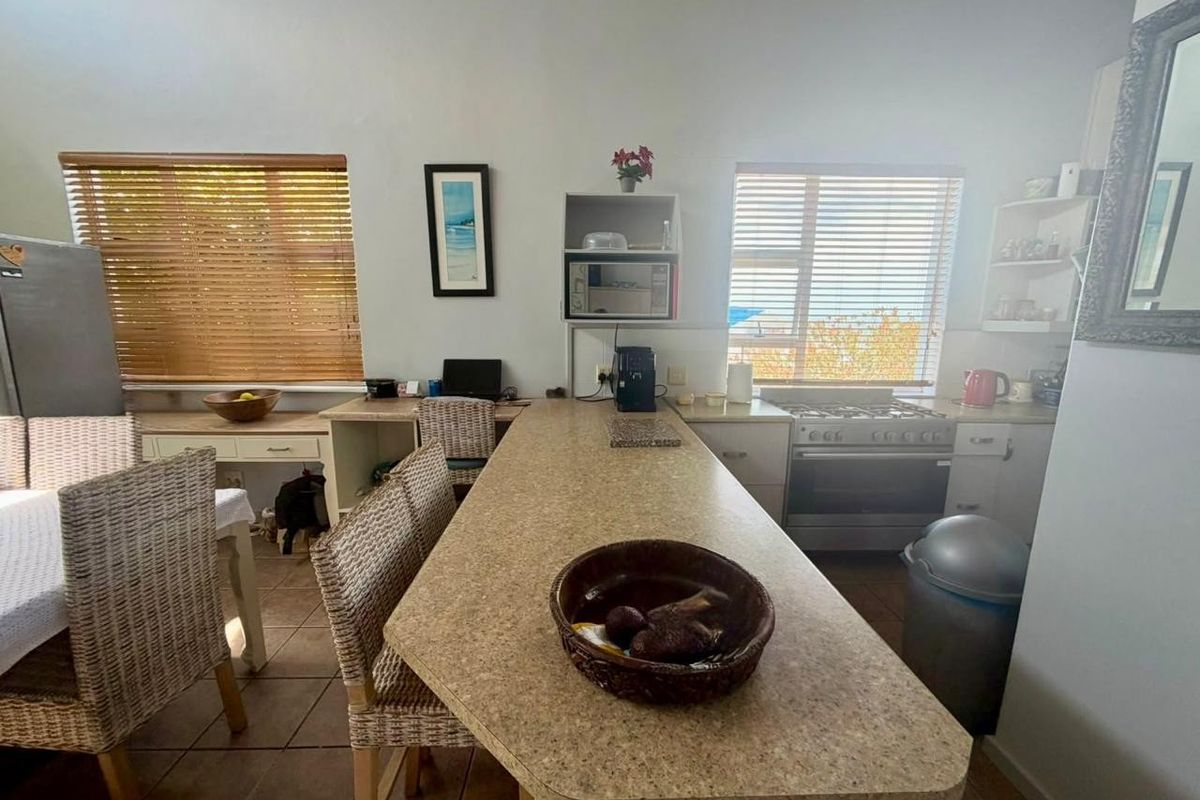 A functional kitchen featuring a central island, gas stove, built-in cabinetry, and an integrated desk area with tiled flooring and natural light.