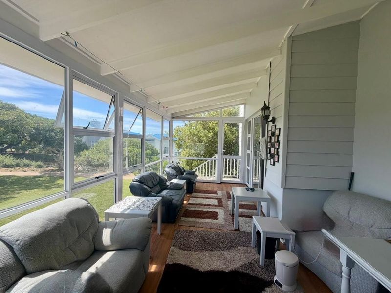 A bright, enclosed sunroom or patio featuring large windows, timber flooring, and exposed beam ceilings, offering a comfortable space with garden views.