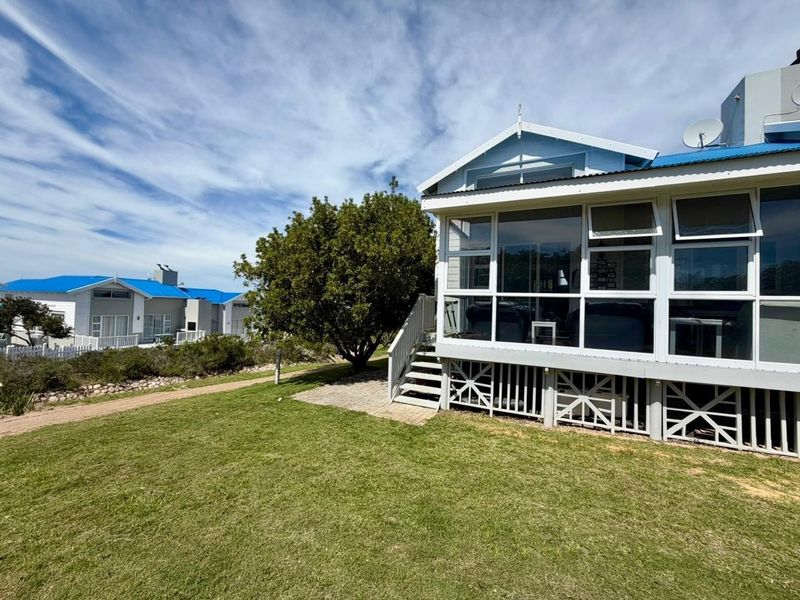 Rear view of the property featuring an elevated enclosed sunroom with a metal roof, timber staircase, and access to a landscaped garden area.
