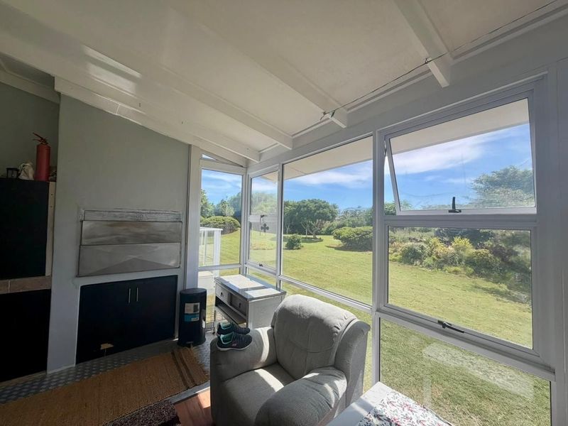 A sun-filled enclosed patio featuring large windows with garden views, exposed beam ceilings, and a built-in fireplace.