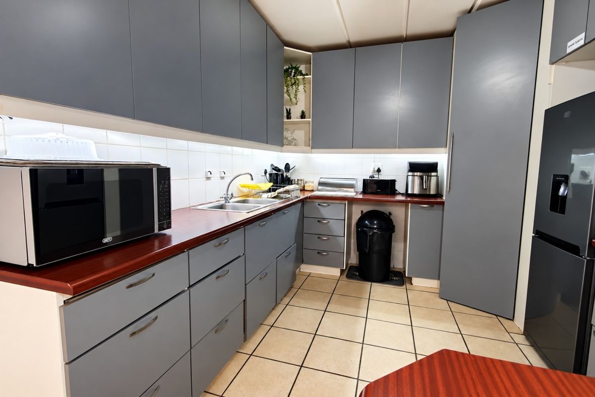A functional kitchen featuring grey cabinetry, laminate countertops, tiled backsplash, and tiled flooring, providing ample storage and workspace.