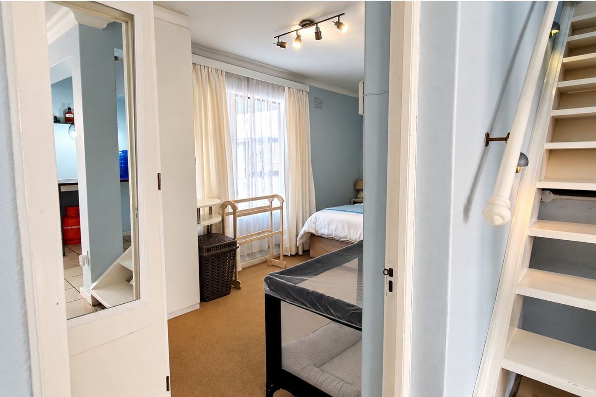 A bedroom featuring a built-in wardrobe, staircase access, and track lighting, viewed from an adjacent hallway.