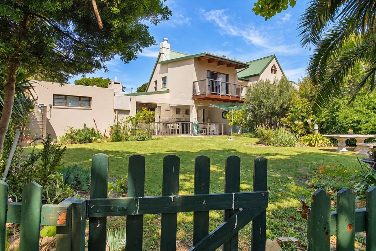 Rear view of the house featuring a spacious garden, a wooden deck, and an upper-level balcony with a chimney.