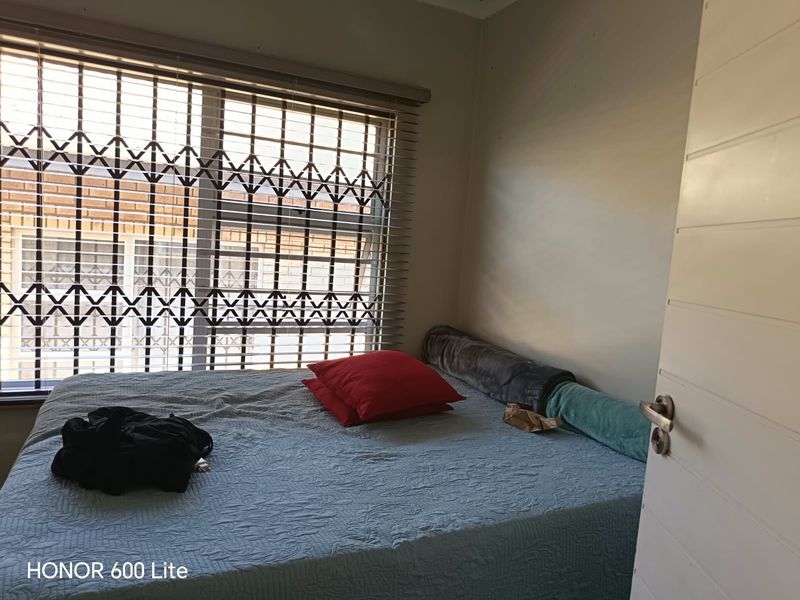 A bedroom featuring a window with fitted security gate and venetian blinds, providing natural light and security.