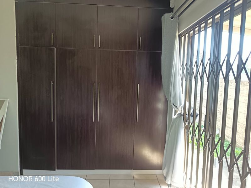 Bedroom featuring dark wood built-in cupboards, tiled flooring, and a sliding door with a security gate.