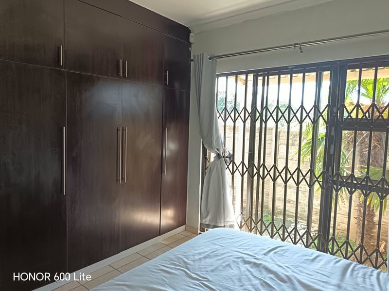Bedroom featuring dark wood built-in cupboards, tiled flooring, and a sliding door with a security gate leading to the exterior.