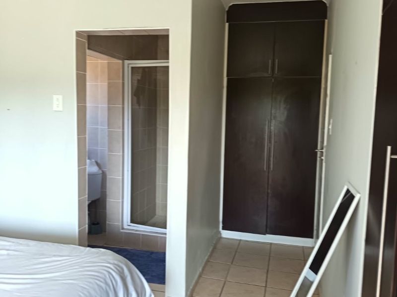 Bedroom featuring tiled flooring, built-in dark wood cupboards, and an adjoining en-suite shower room.
