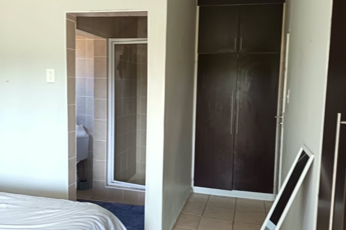 Bedroom featuring tiled flooring, built-in dark wood cupboards, and an adjoining en-suite shower room.