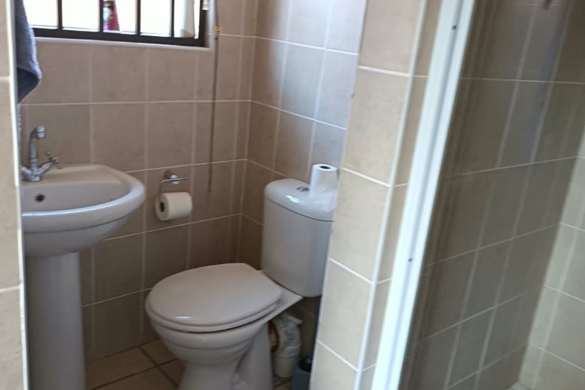 A functional bathroom featuring a pedestal basin, toilet, and a shower enclosure with neutral ceramic tiling throughout.