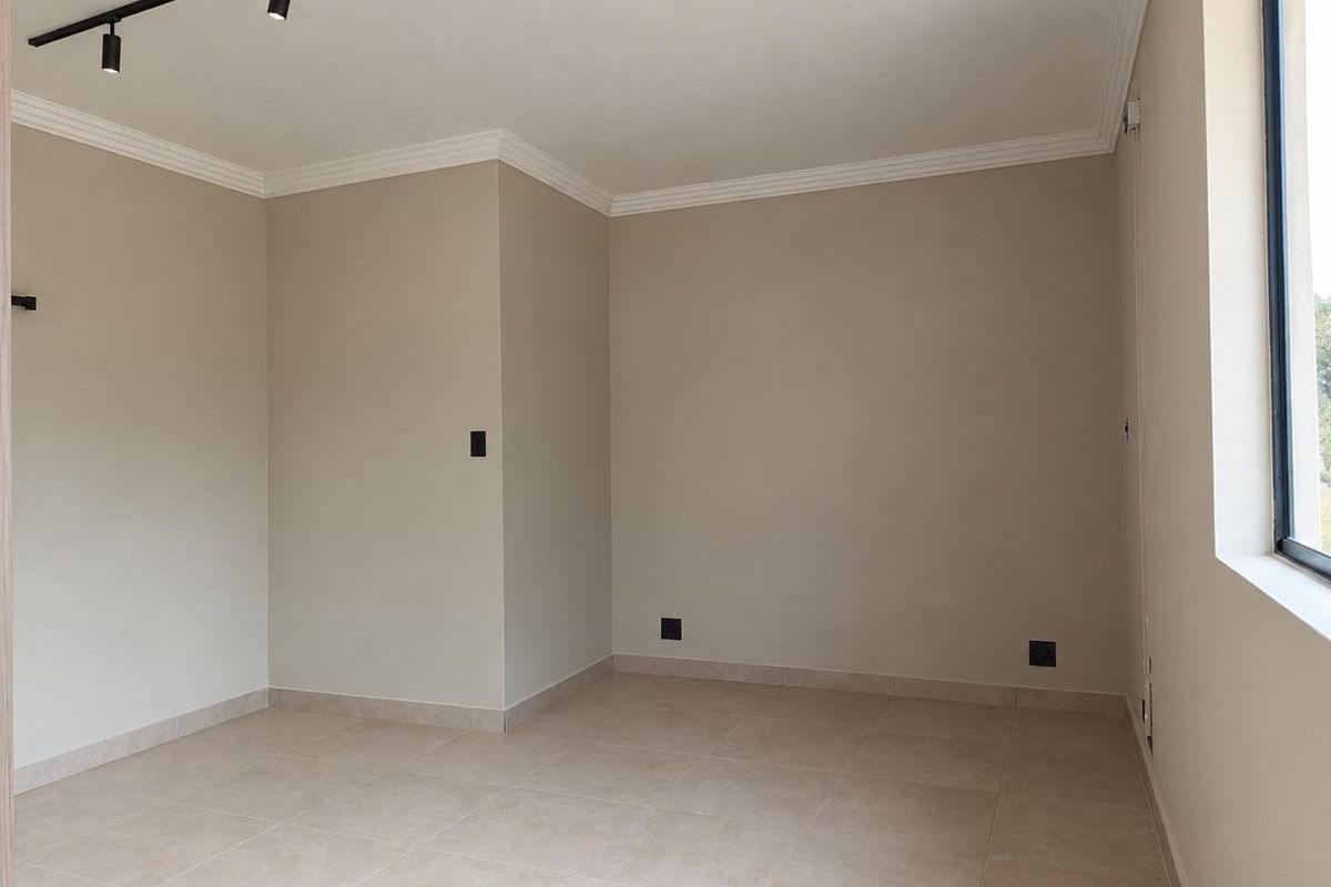 A bright, empty living area featuring neutral tiled flooring, modern track lighting, and clean finishes, ready for personalization.