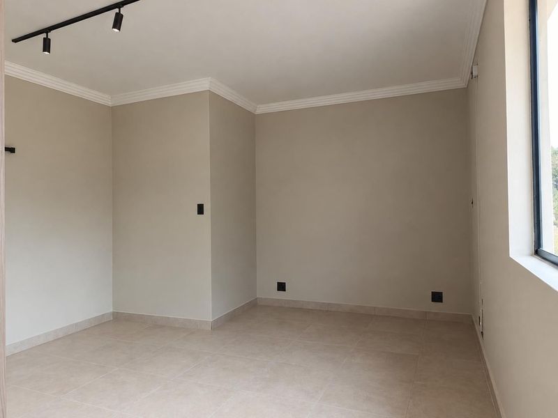 A bright, empty living area featuring neutral tiled flooring, modern track lighting, and clean finishes, ready for personalization.