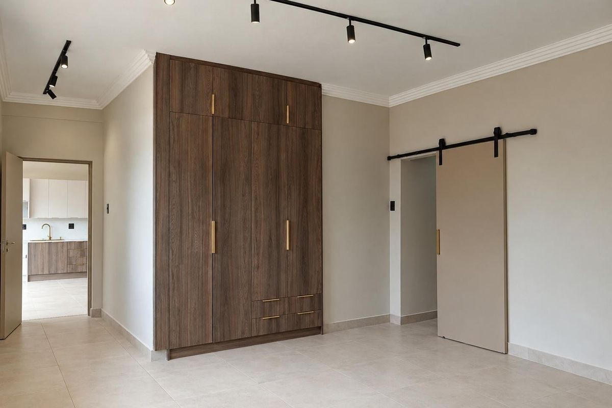 A modern, minimalist bedroom featuring a large built-in wood-finish wardrobe, sleek track lighting, and a contemporary sliding barn door.