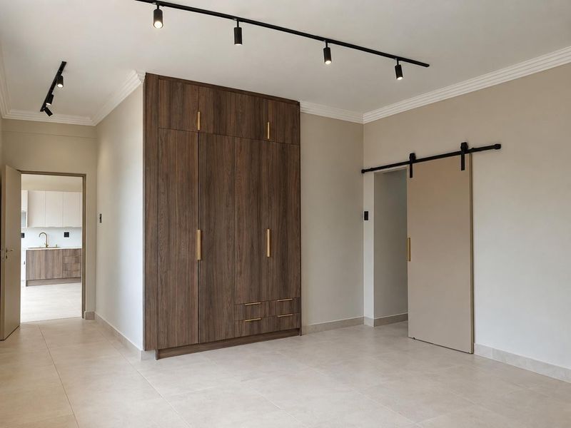 A modern, minimalist bedroom featuring a large built-in wood-finish wardrobe, sleek track lighting, and a contemporary sliding barn door.
