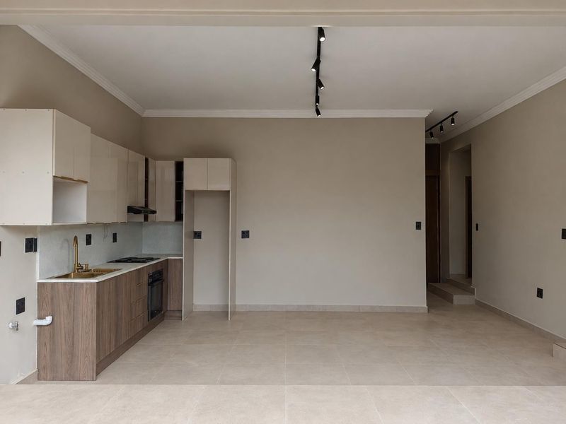 A modern, empty kitchen featuring sleek cabinetry, integrated appliances, tiled flooring, and contemporary track lighting, offering a clean and functional space.