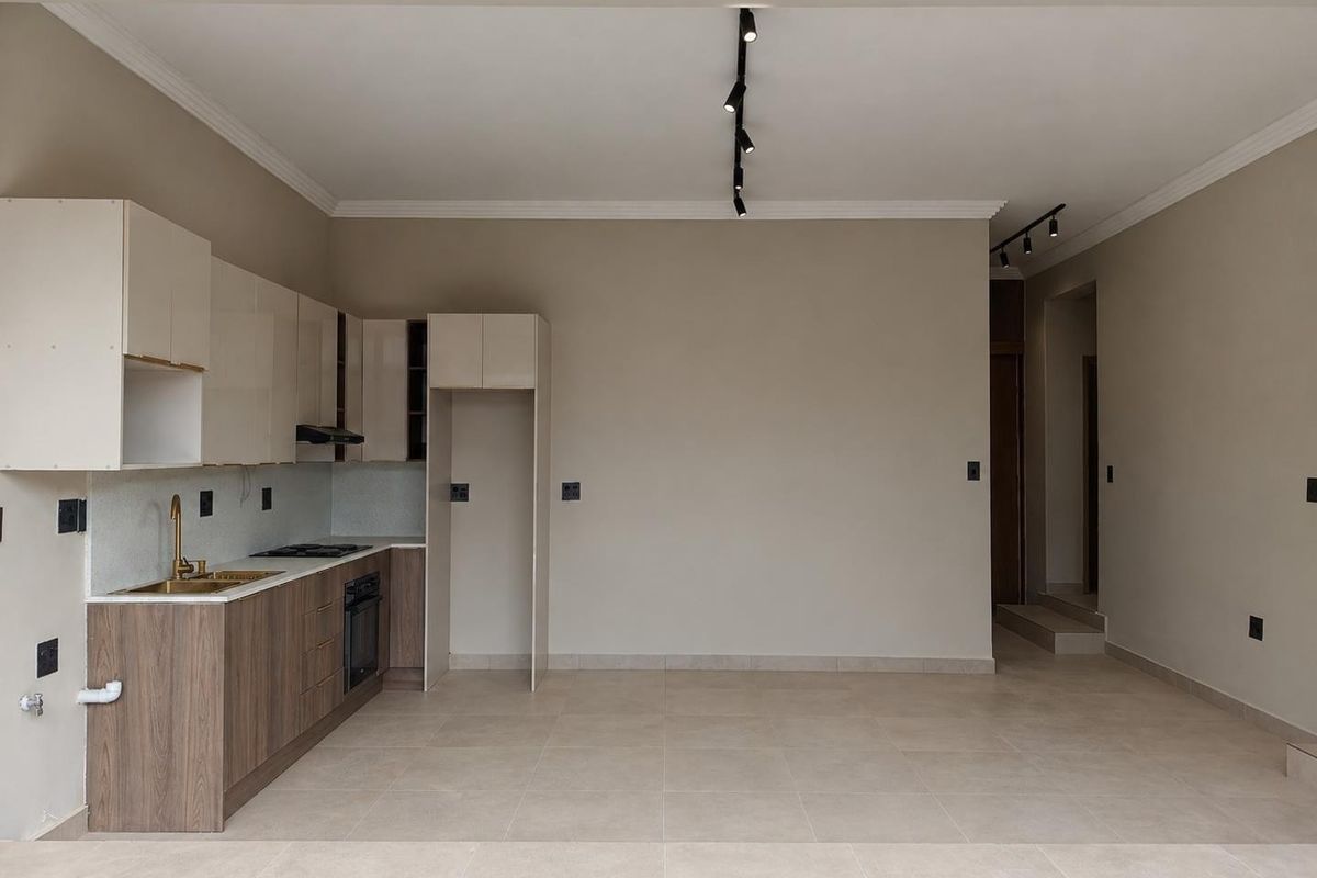A modern, empty kitchen featuring sleek cabinetry, integrated appliances, tiled flooring, and contemporary track lighting, offering a clean and functional space.