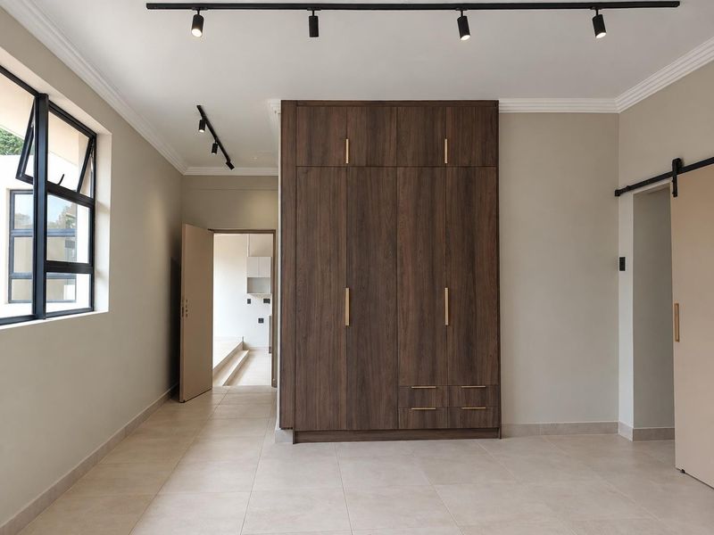 A bright, modern bedroom featuring sleek built-in wooden cupboards, contemporary track lighting, tiled floors, and a stylish sliding barn door.