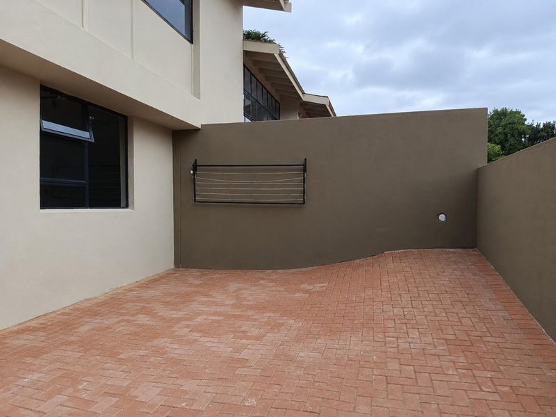 A private rear courtyard featuring neat brick paving, a boundary wall, and a wall-mounted drying rack.