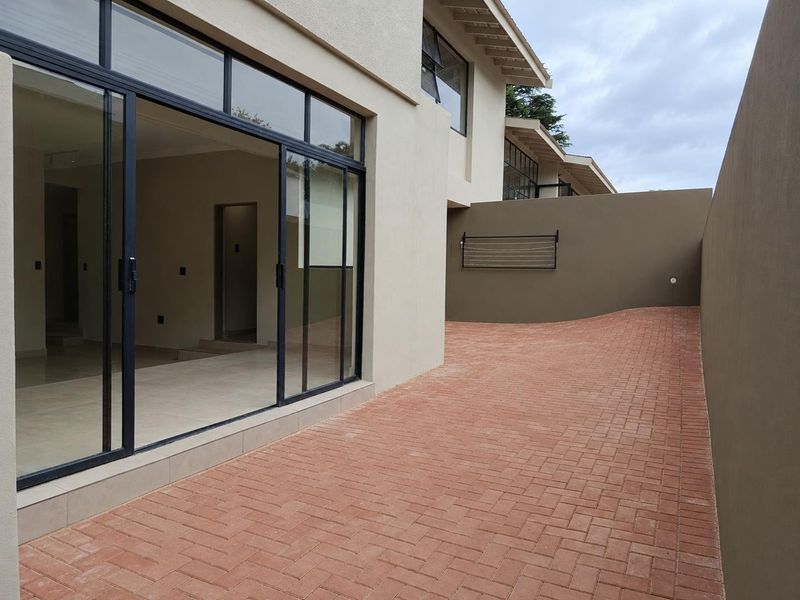 A clean rear exterior area featuring a paved courtyard, boundary wall, and large sliding glass doors providing access to the interior living space.