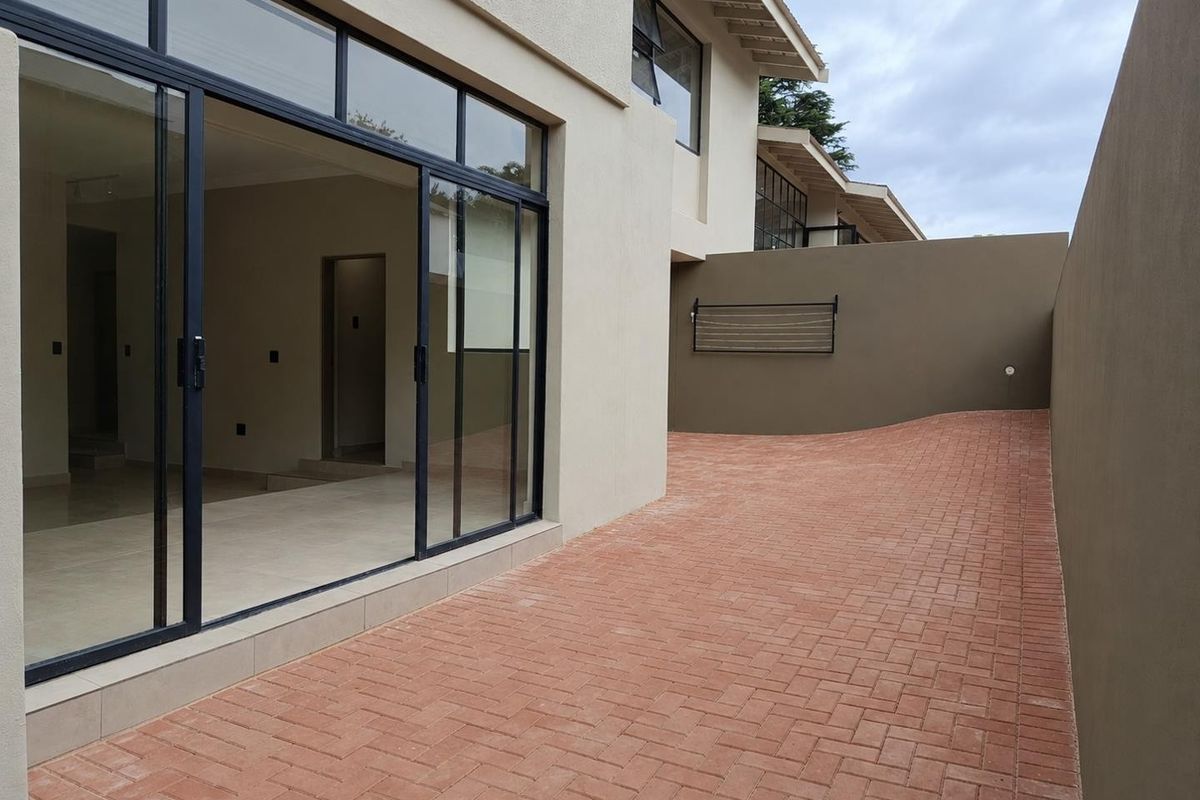 A clean rear exterior area featuring a paved courtyard, boundary wall, and large sliding glass doors providing access to the interior living space.