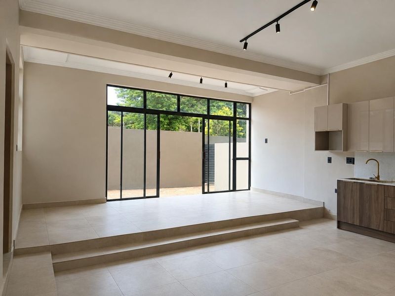 Modern open-plan living area featuring a raised floor platform, sleek track lighting, and large sliding glass doors opening to the rear exterior.