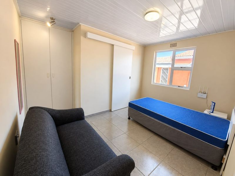 A bedroom featuring tiled flooring, built-in cupboards, and a sliding door, providing a functional and well-lit living space.