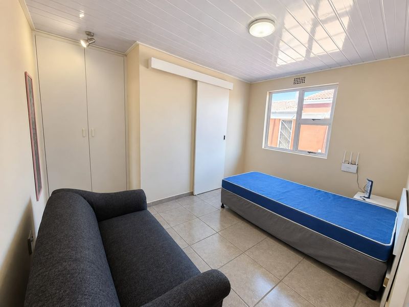 A functional bedroom featuring tiled flooring, a built-in wardrobe, and a sliding door, providing a clean and practical living space.