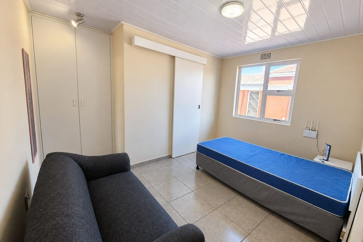 A functional bedroom featuring tiled flooring, a built-in wardrobe, and a sliding door, providing a clean and practical living space.