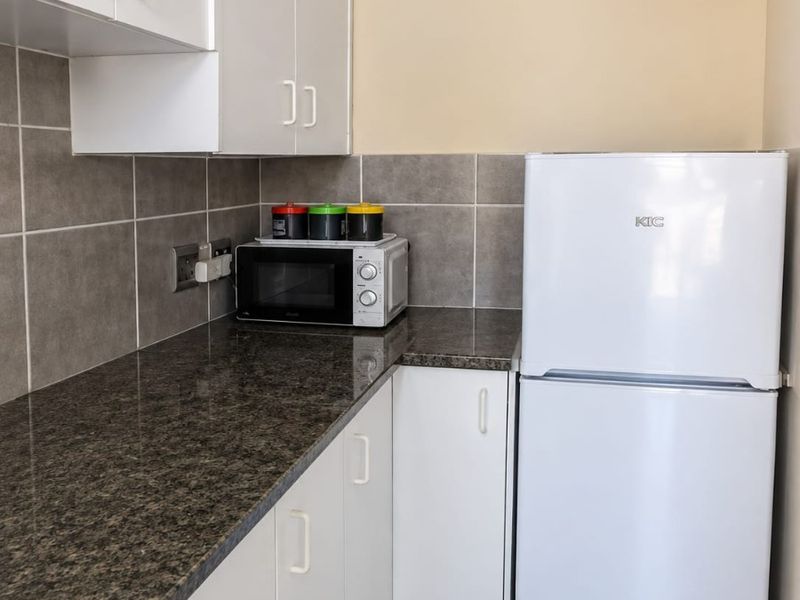 A compact kitchen featuring white cabinetry, granite countertops, and neutral tiled backsplash and flooring, providing a functional and clean workspace.