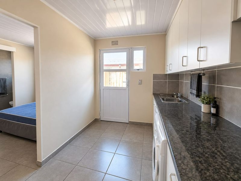 A clean and functional laundry area featuring granite countertops, a stainless steel sink, tiled flooring, and ample built-in cabinetry.
