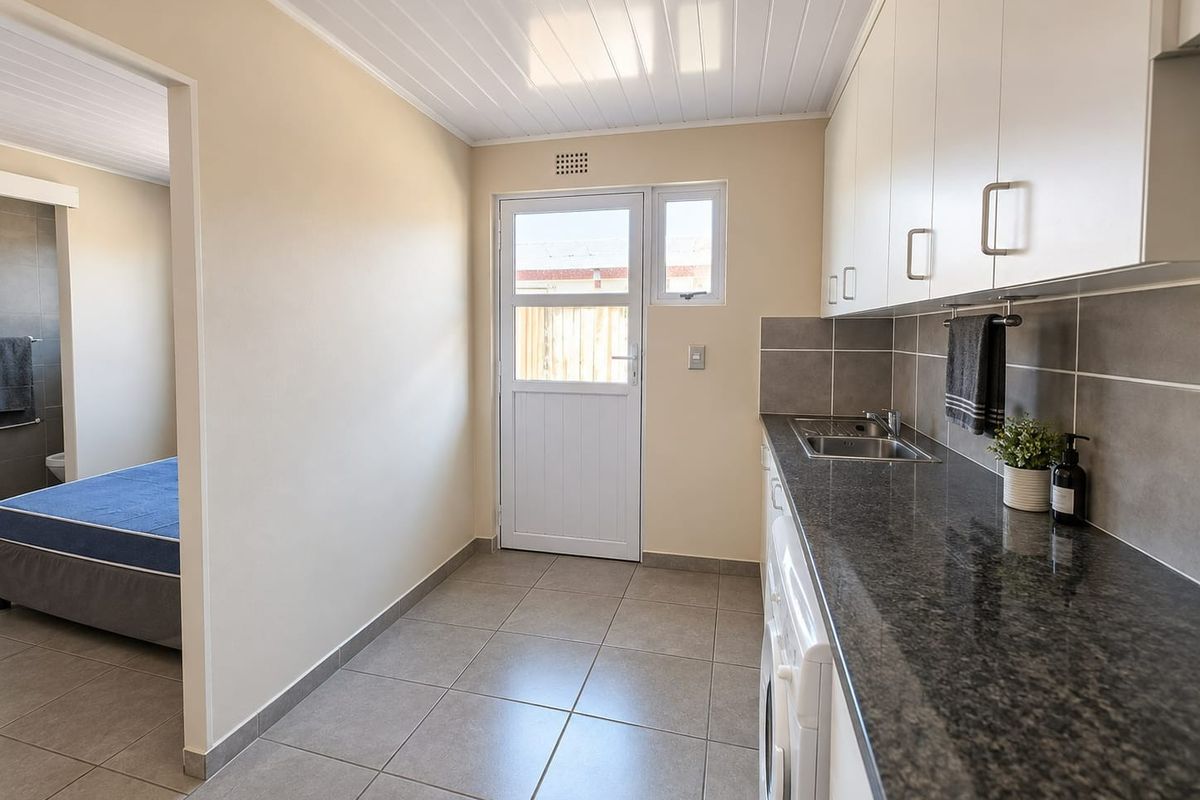 A clean and functional laundry area featuring granite countertops, a stainless steel sink, tiled flooring, and ample built-in cabinetry.