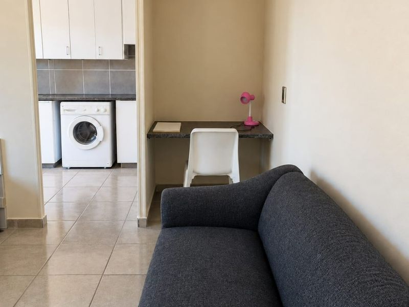 Open plan living area featuring tiled flooring and a built-in desk, with an adjacent kitchen area visible through the doorway.