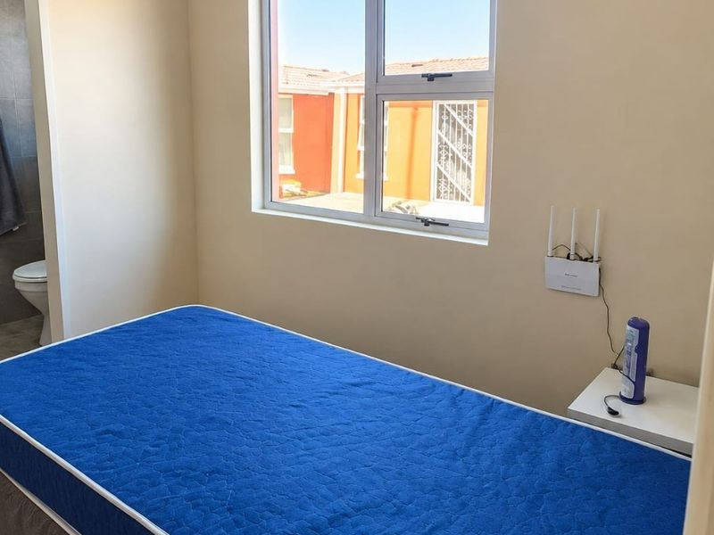 A bedroom featuring tiled flooring, a large aluminium window, and direct access to an en-suite bathroom.