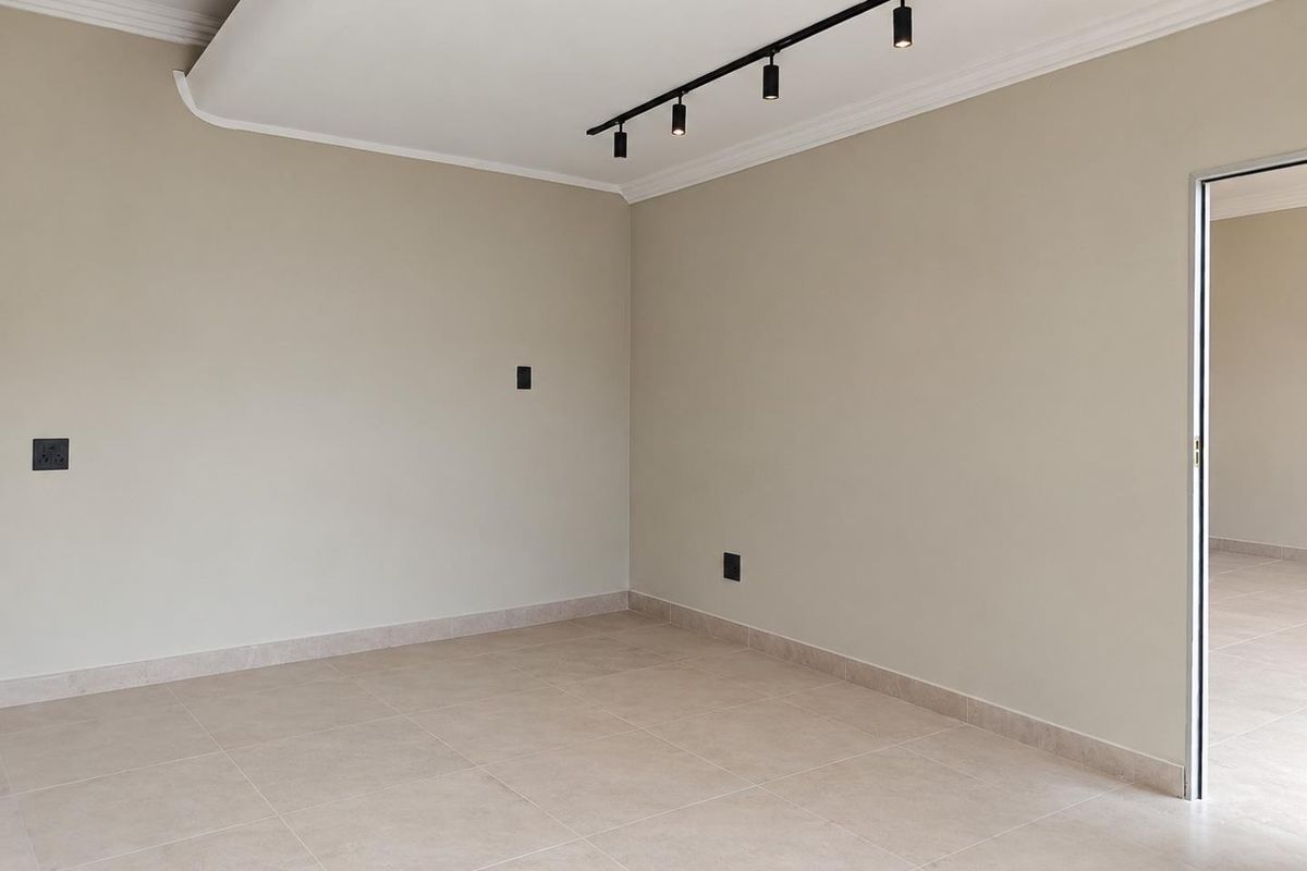 A bright, empty living area featuring neutral tiled flooring, modern track lighting, and a clean, minimalist aesthetic ready for personalization.