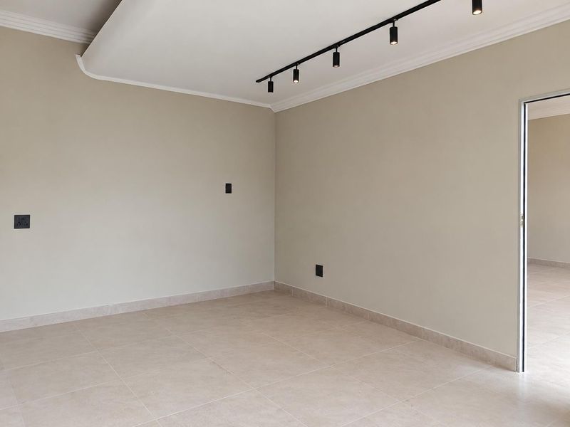 A bright, empty living area featuring neutral tiled flooring, modern track lighting, and a clean, minimalist aesthetic ready for personalization.