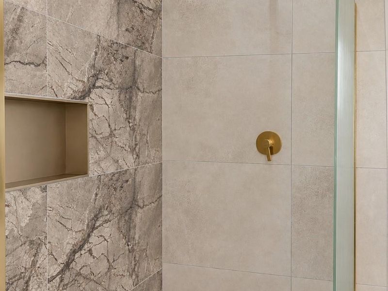 Modern walk-in shower featuring premium marble-look wall tiles, brushed brass fixtures, a built-in niche, and a sleek glass screen.