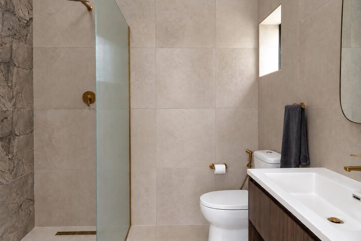 Modern bathroom featuring a walk-in shower with glass screen, brass fixtures, wall-mounted toilet, and a sleek vanity cabinet with integrated basin.