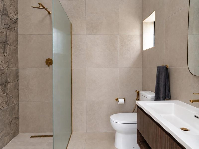 Modern bathroom featuring a walk-in shower with glass screen, brass fixtures, wall-mounted toilet, and a sleek vanity cabinet with integrated basin.