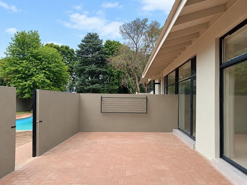 A clean, paved outdoor patio area featuring a wall-mounted drying rack, sliding glass door access, and views toward the garden and pool area.
