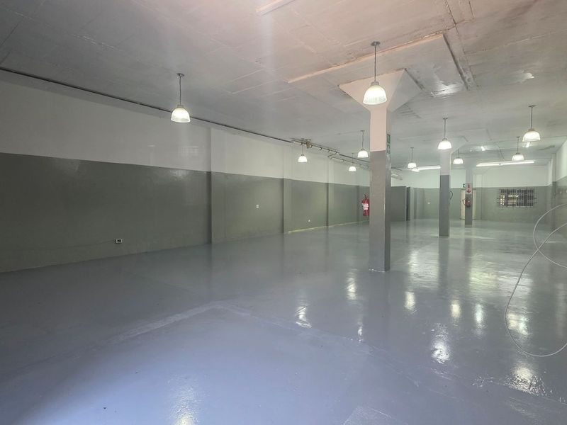 Spacious open-plan industrial warehouse area featuring polished epoxy flooring, support columns, and functional pendant lighting throughout the expansive interior space.