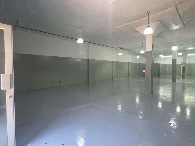 Spacious industrial utility area featuring polished epoxy flooring, structural support columns, and functional pendant lighting, suitable for storage or workshop use.