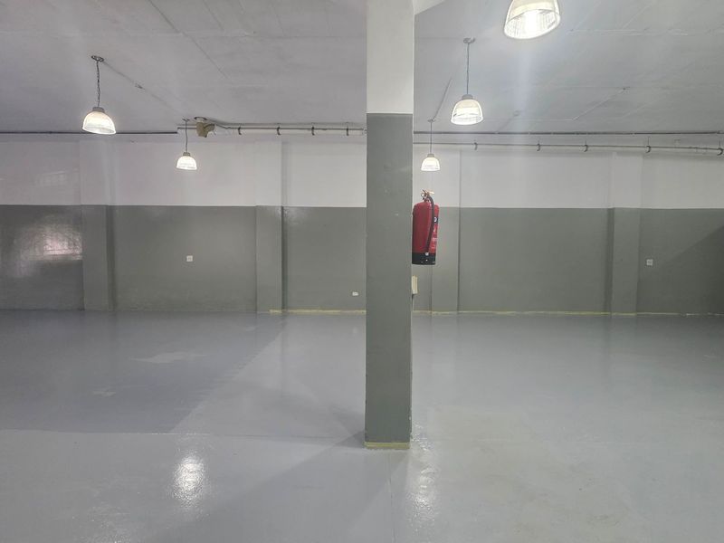 A spacious, open-plan industrial utility area featuring durable epoxy flooring, structural columns, and functional pendant lighting, suitable for storage or workshop use.
