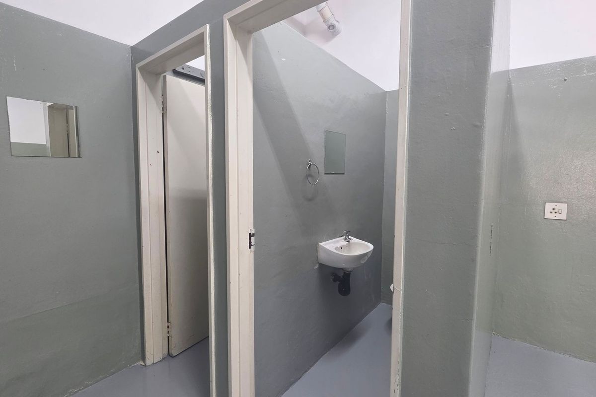 A functional industrial-style bathroom featuring a wall-mounted basin, mirror, and simple painted finishes.