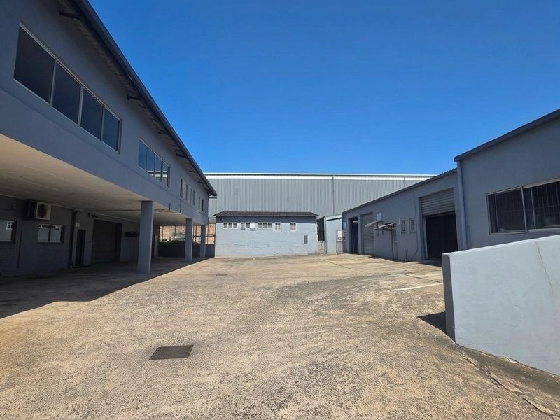 Spacious industrial yard area featuring concrete paving, multiple roller shutter access points, and surrounding warehouse structures with metal cladding.