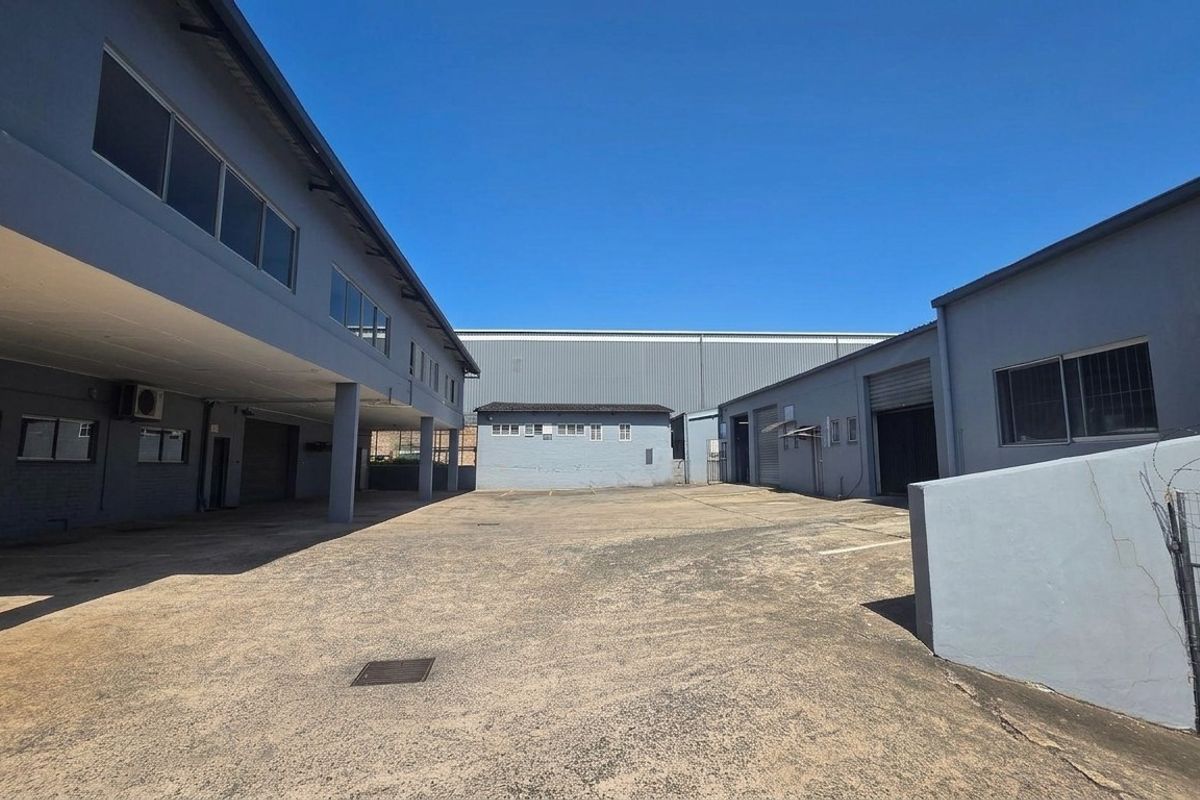 Spacious industrial yard area featuring concrete paving, multiple roller shutter access points, and surrounding warehouse structures with metal cladding.